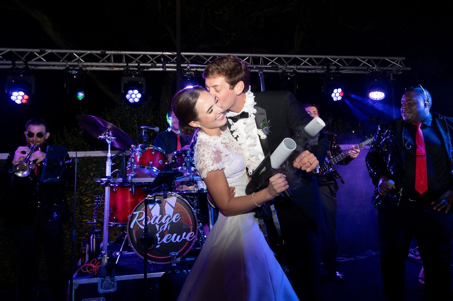 Couples dancing and celebrating at a lively wedding reception with blue stage lighting.
