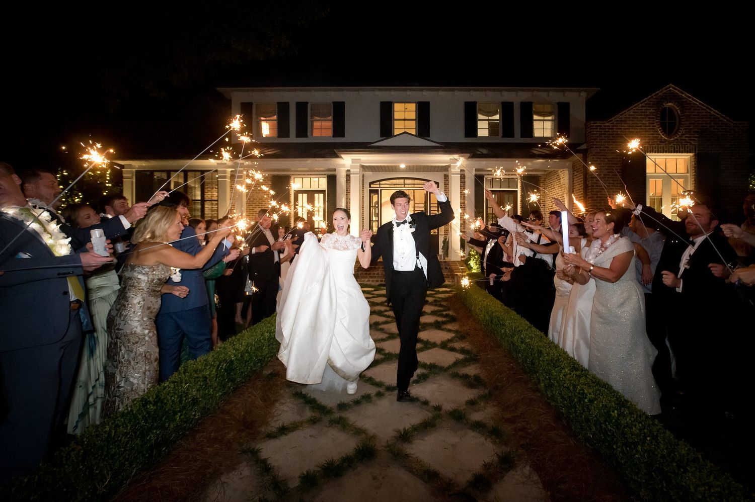 Wedding celebration at night outside a beautifully lit venue with guests dancing.