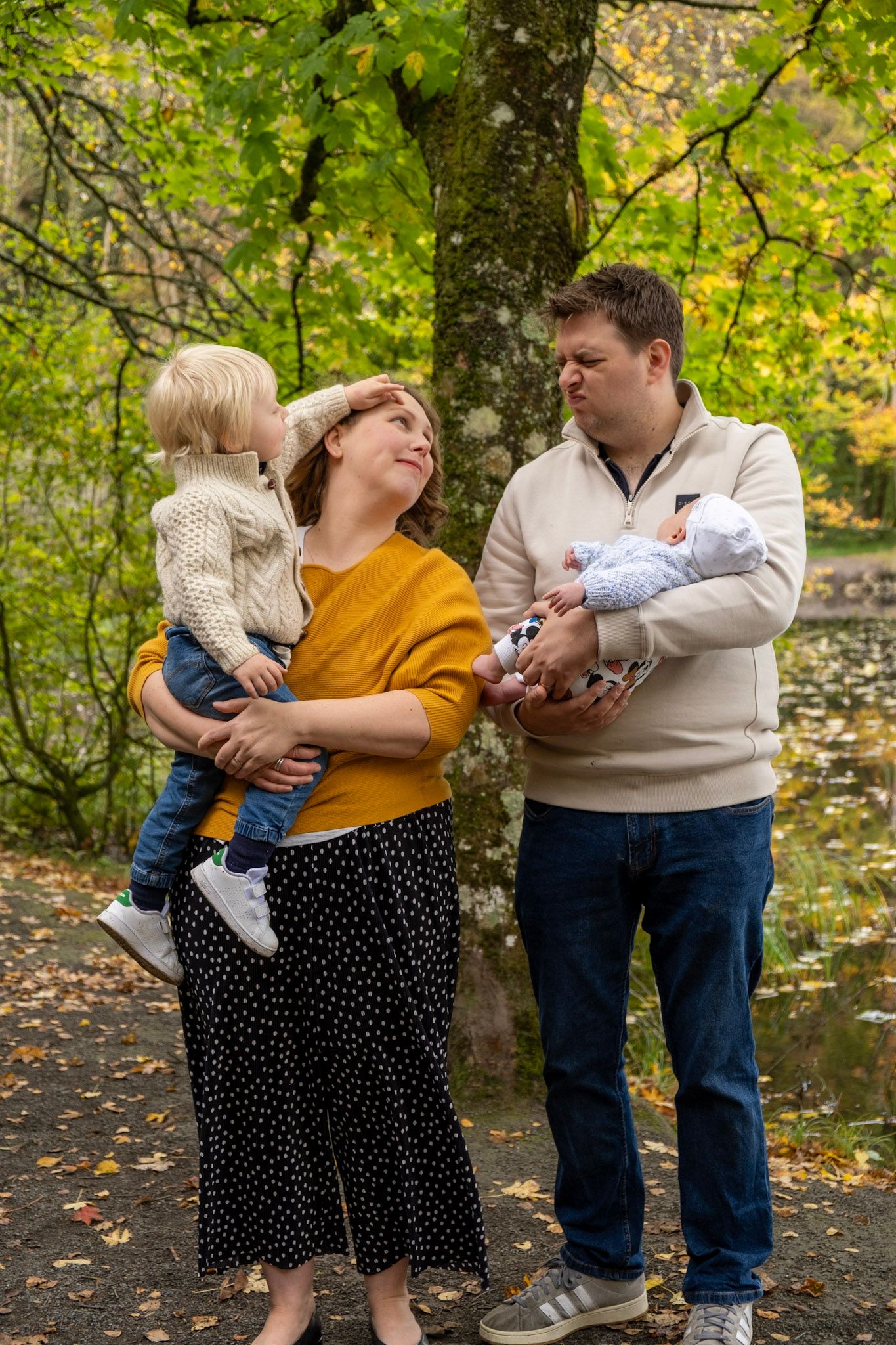 A family shares tender moments together during an autumn photoshoot in a park with golden leaves.