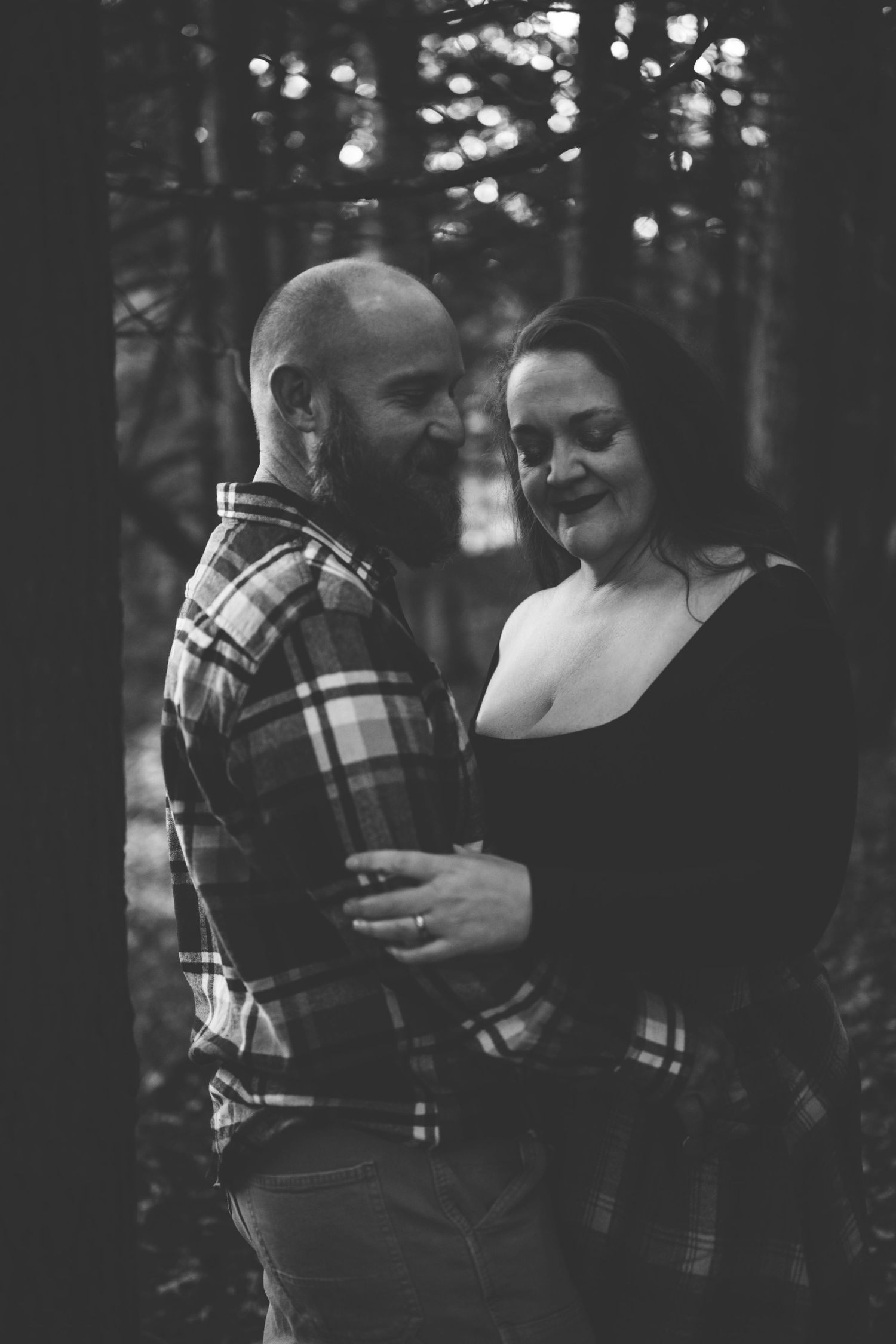 A romantic black and white photo series showing a couple embracing in a wooded setting with bokeh lighting effects.