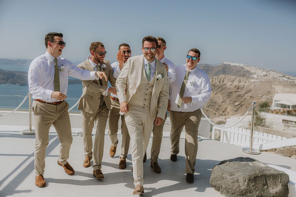 Groomsmen in light suits gather on a terrace overlooking the Mediterranean Sea.