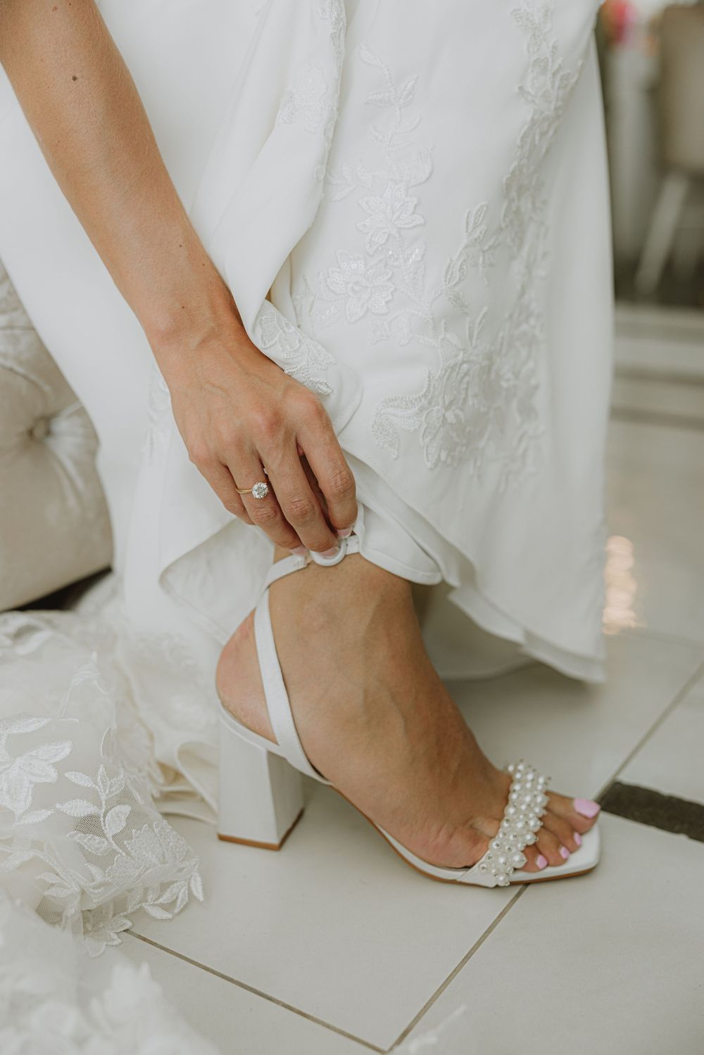 Close-up of bride putting on elegant pearl-embellished wedding shoes.