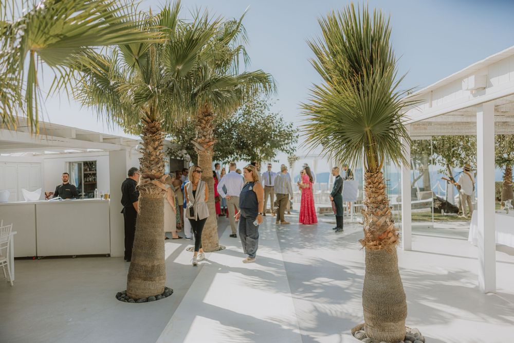 Palm trees line a white-walled Mediterranean venue terrace under bright blue skies.