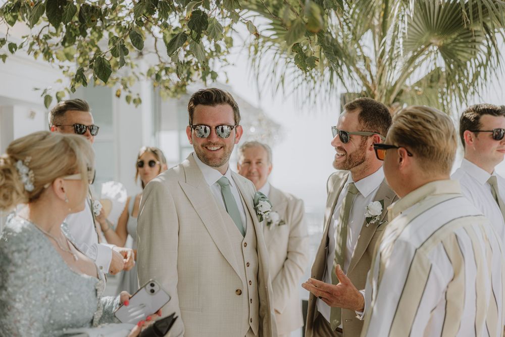 Wedding guests gather under palm trees at an elegant outdoor Mediterranean venue.