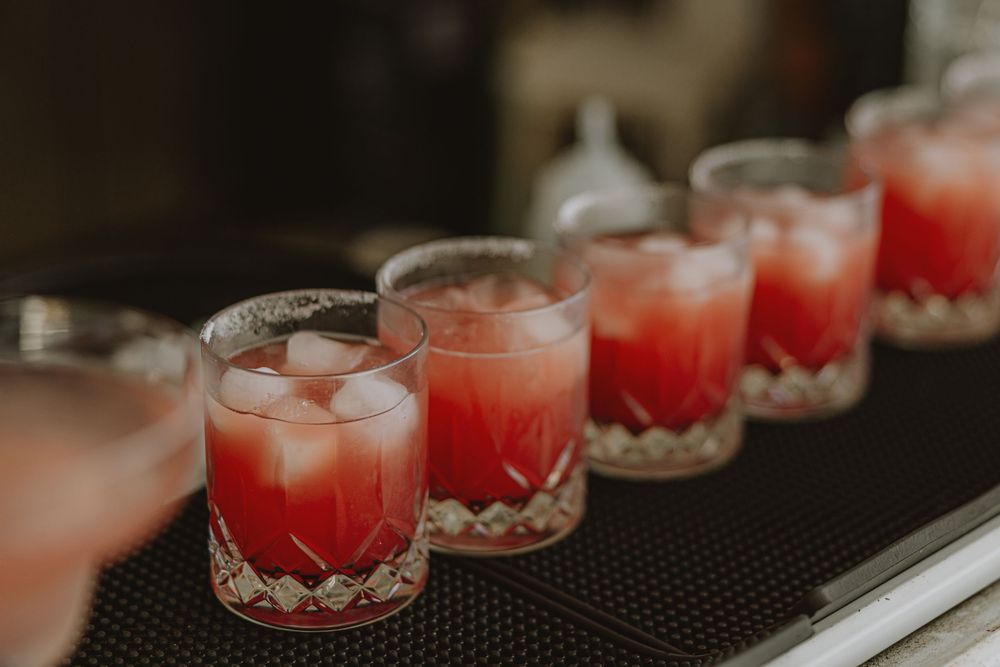 Row of pink cocktails with ice in crystal glasses on black surface.