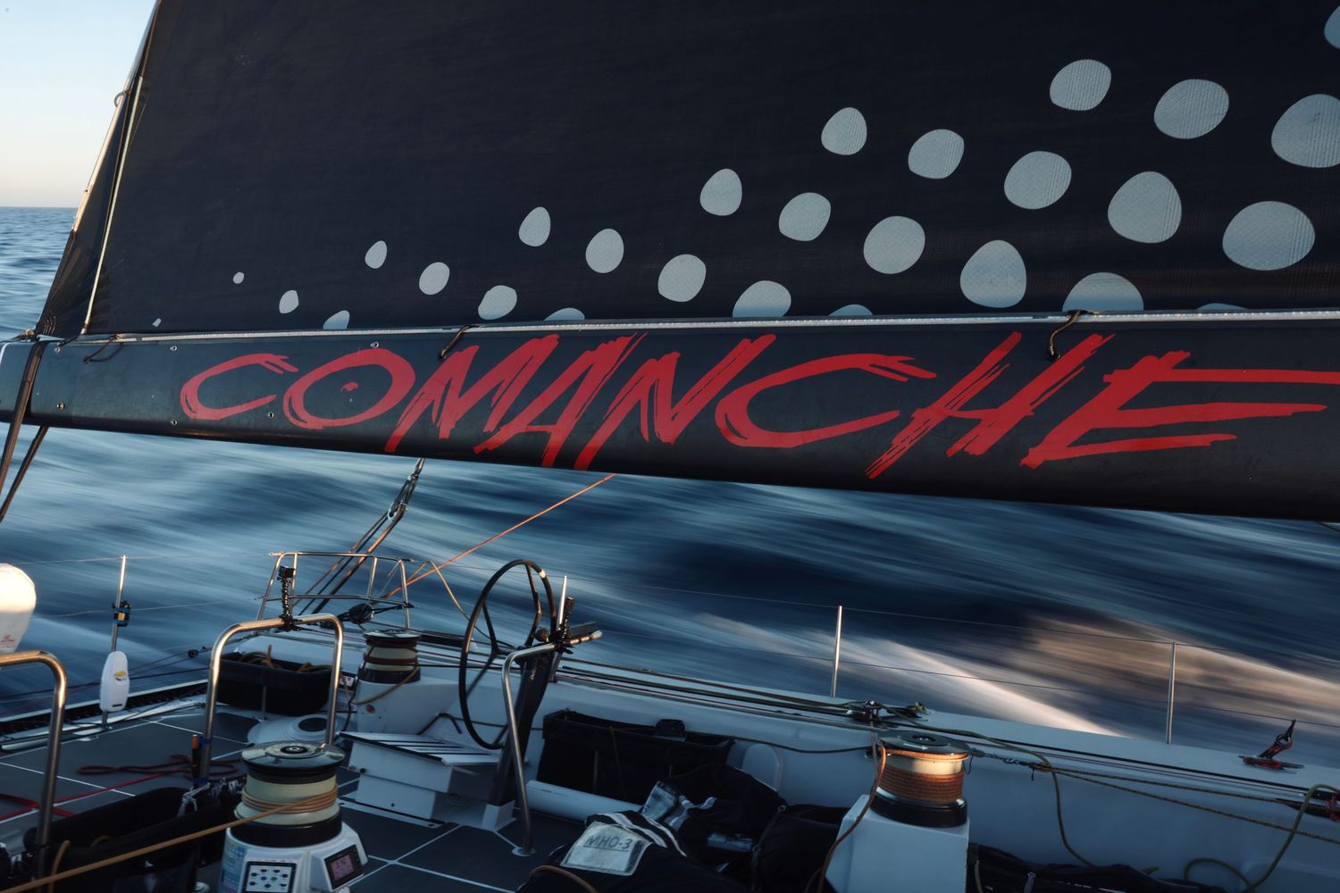Racing yacht with polka dot design cuts through ocean waves.