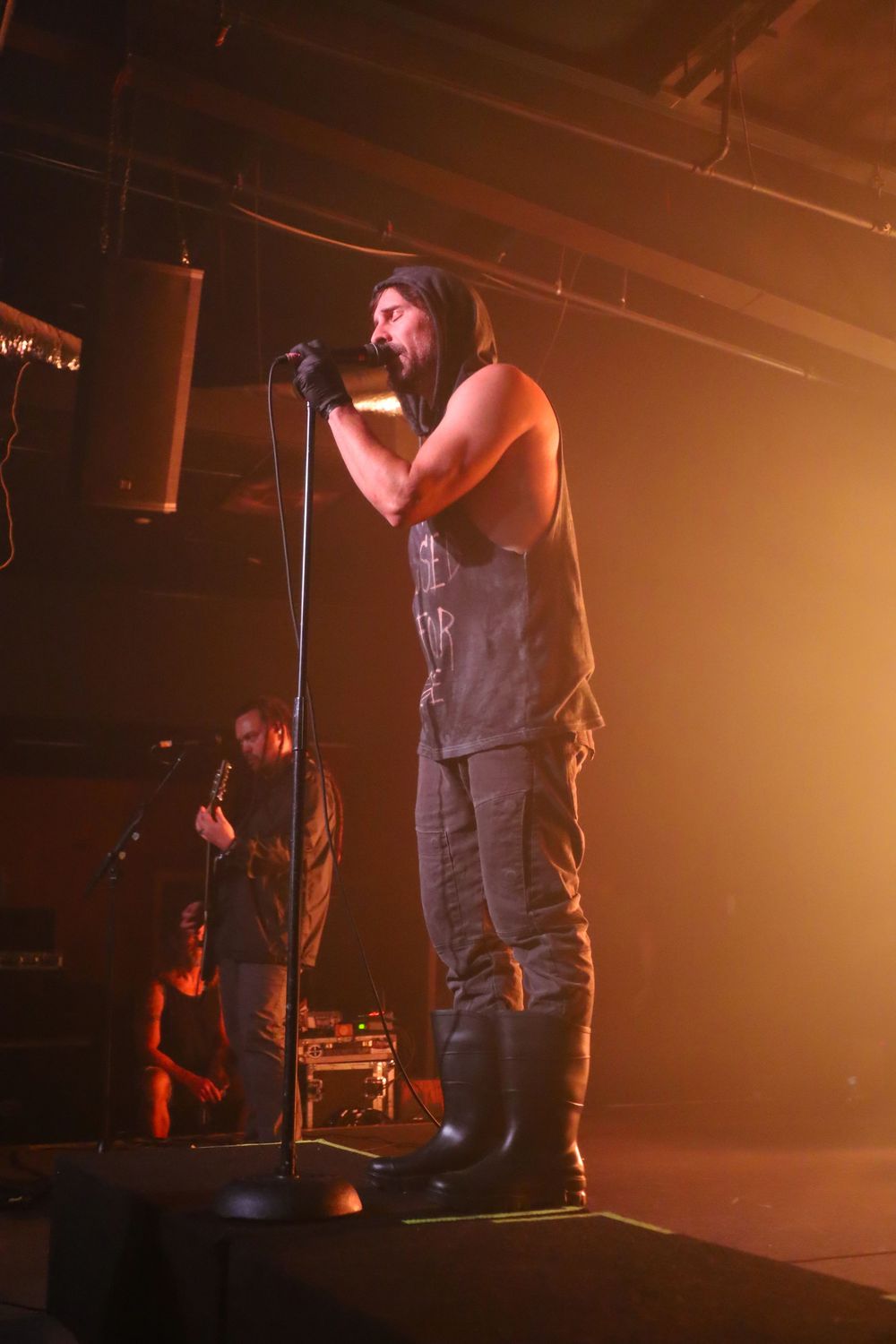 Concert performer on stage illuminated by warm orange lighting during a live music performance.