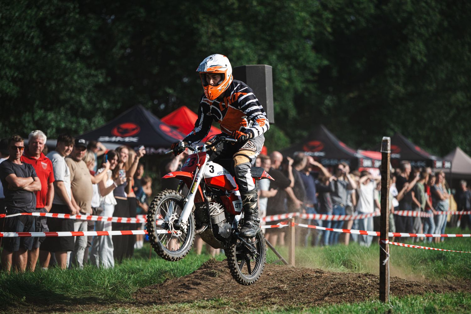 Dirt bike rider performs a jump sequence over a dirt mound during an outdoor motocross competition.