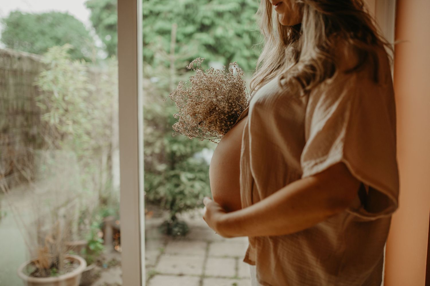 A pregnant woman in casual clothing relaxes on a red couch while cradling her baby bump in warm lighting.