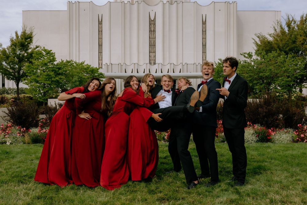 Wedding party lineup wearing deep red dresses and dark suits posed outdoors against green landscaping.