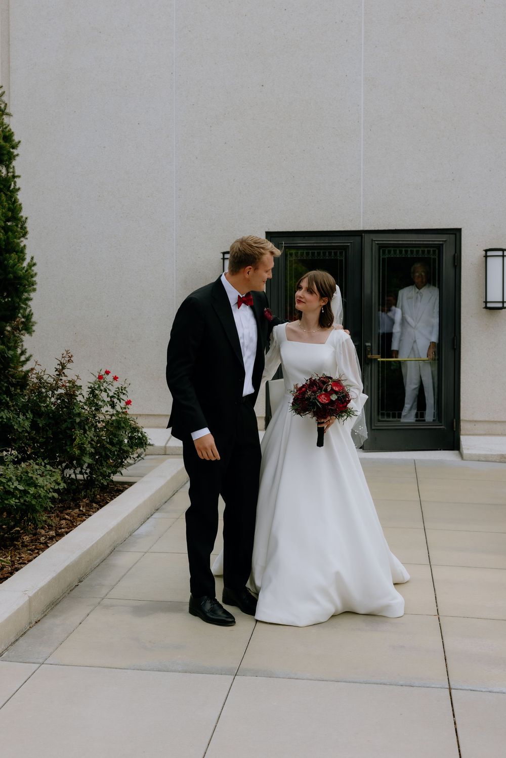 A couple shares a tender moment outside a modern building with dark windows.
