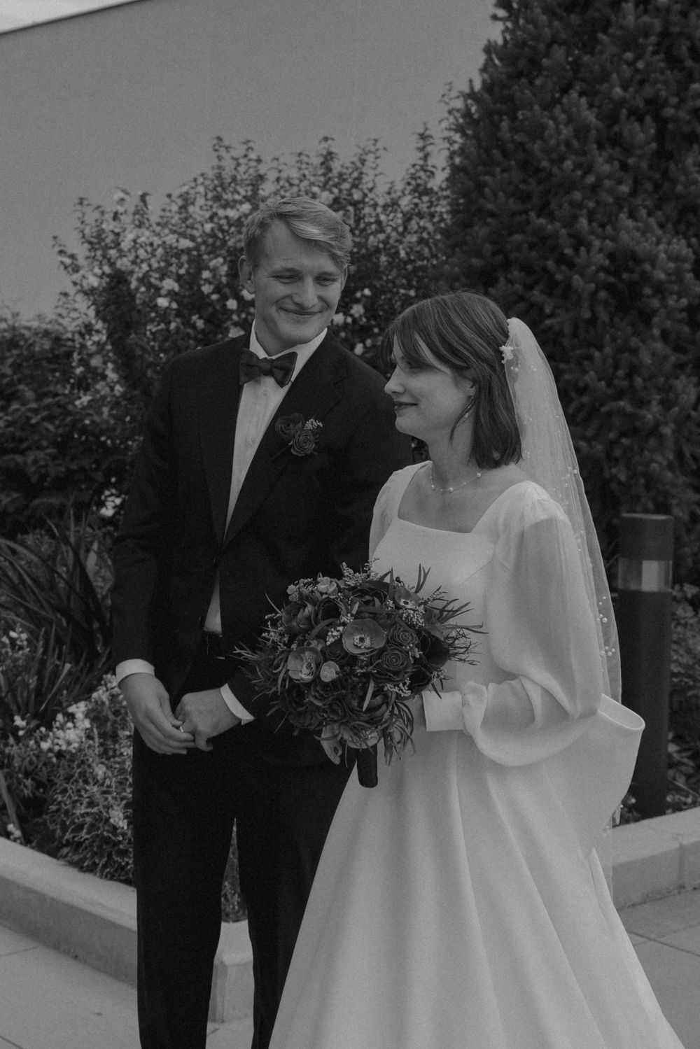 A couple in formal wedding attire shares a joyful moment together outdoors on their special day.
