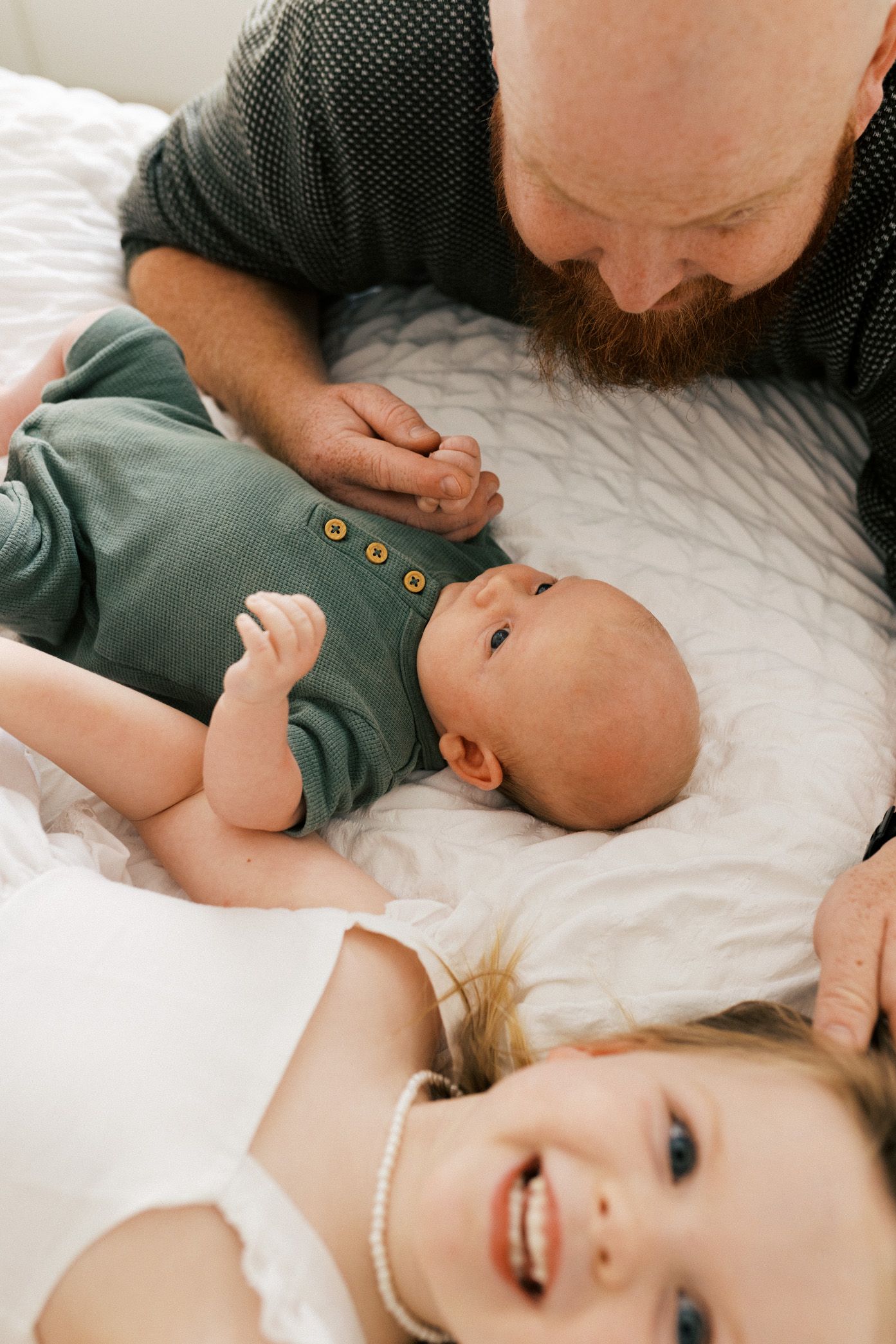A family shares a tender moment together while lying on white bedding.