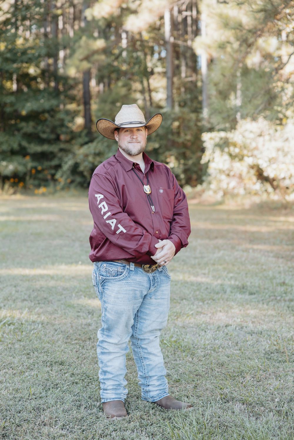 Person in maroon shirt and cowboy hat standing on grass in outdoor setting.