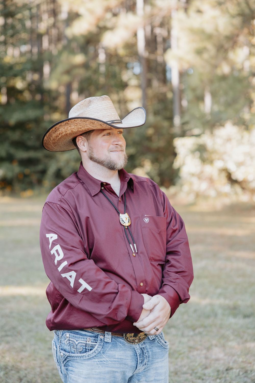 Person in maroon shirt and cowboy hat posing outdoors in casual western attire.