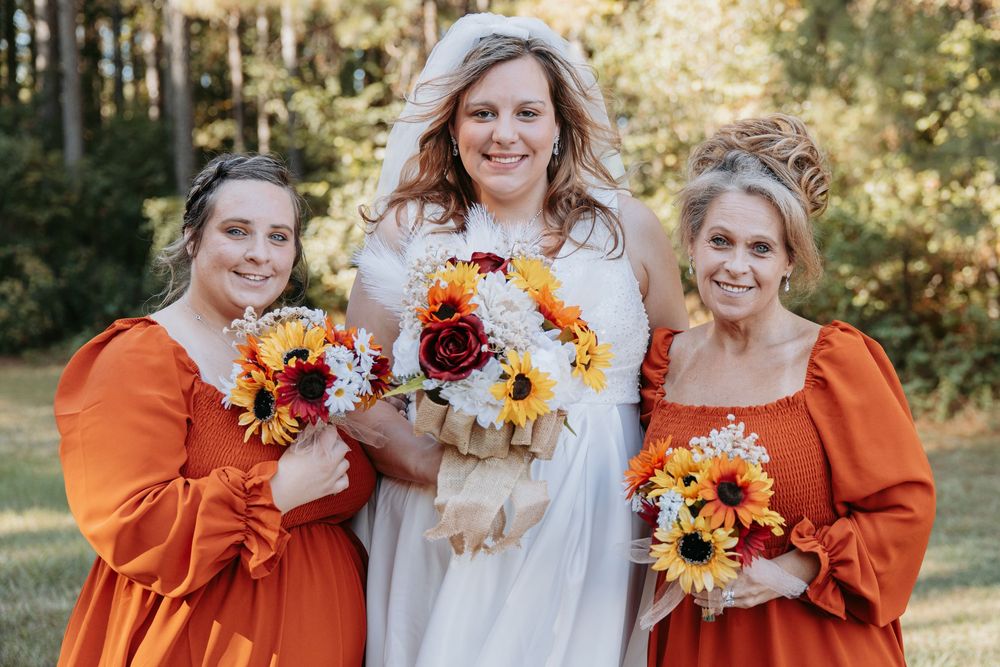 Wedding party in orange bridesmaid dresses and white bridal gown holding autumn-themed bouquets.