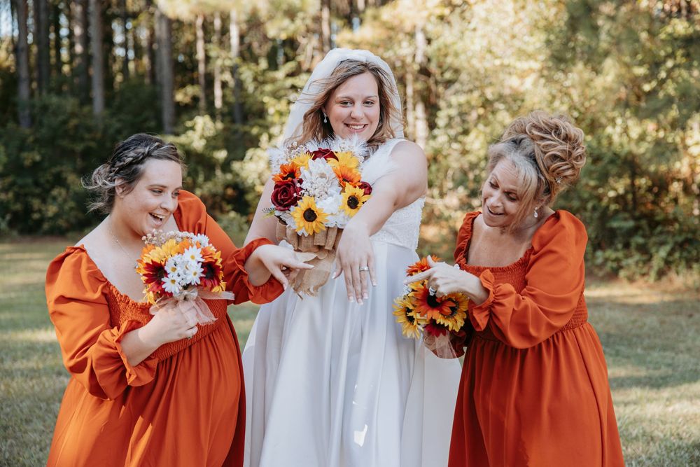 Bridesmaids in burnt orange dresses with bride in white holding sunflower bouquets.