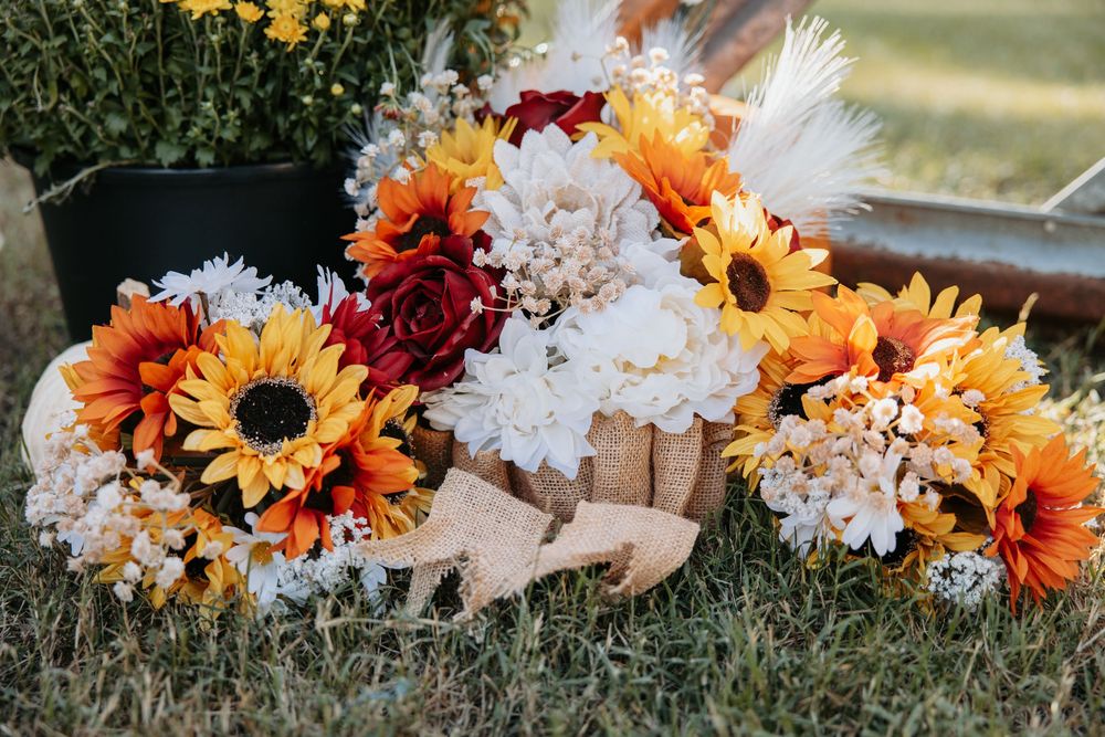 Colorful autumn floral arrangement with sunflowers, daisies, and orange blooms laid on grass.