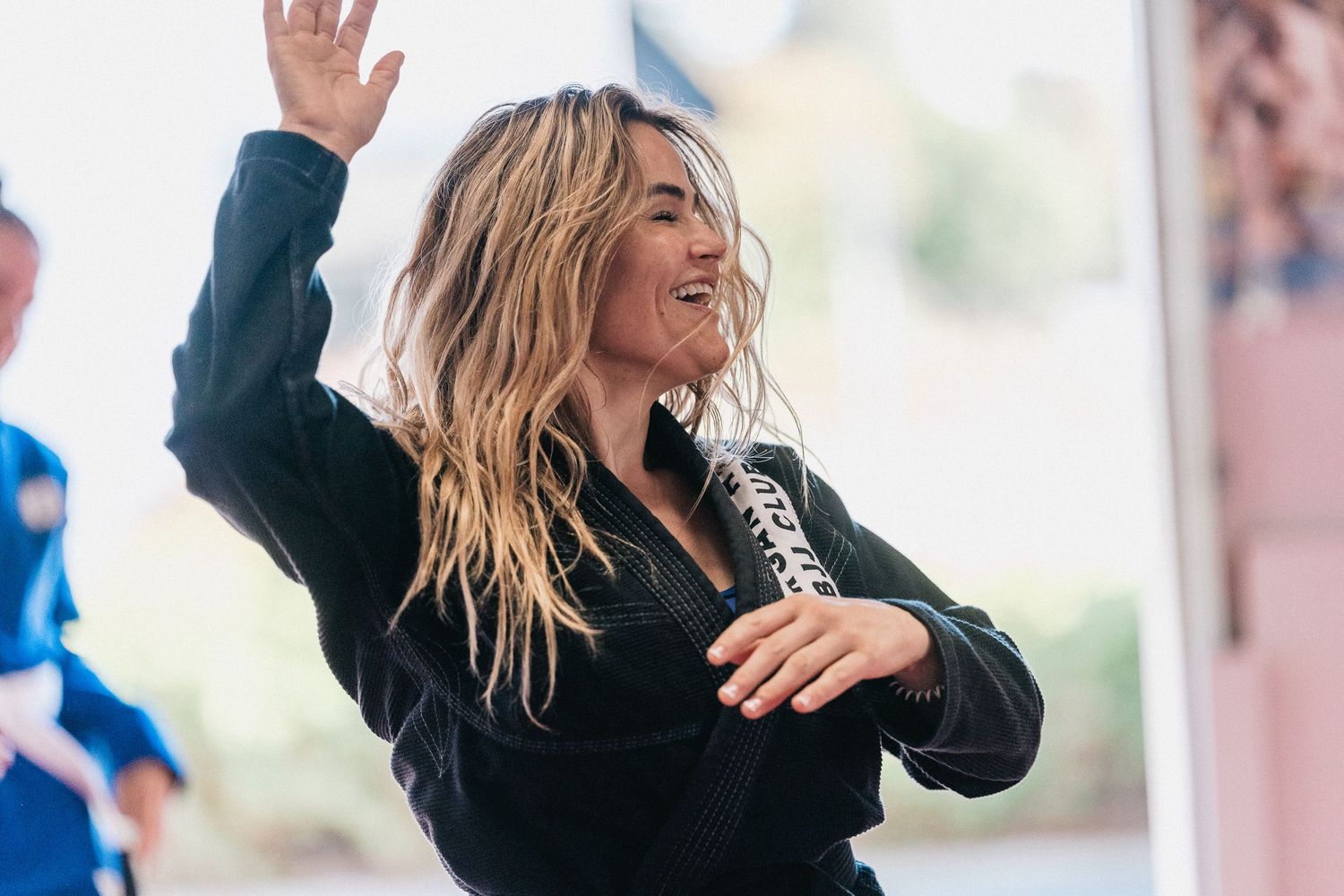 Woman in black top laughing and dancing with messy blonde hair against blurred background.