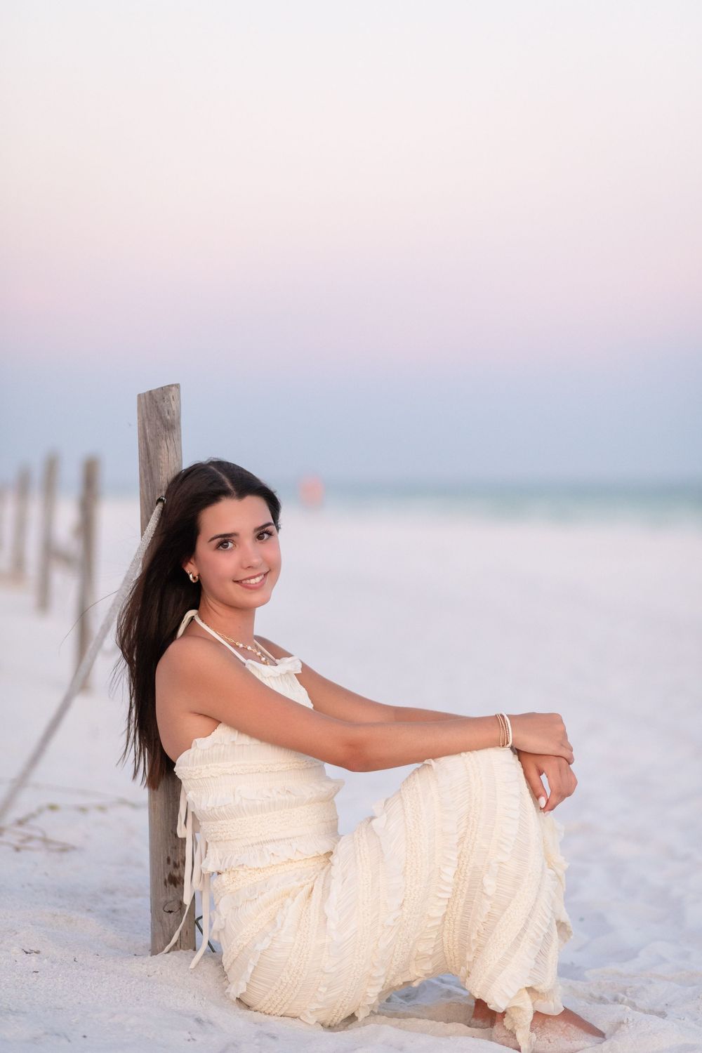 Person in white lace dress poses elegantly on pristine white sand beach at dusk.