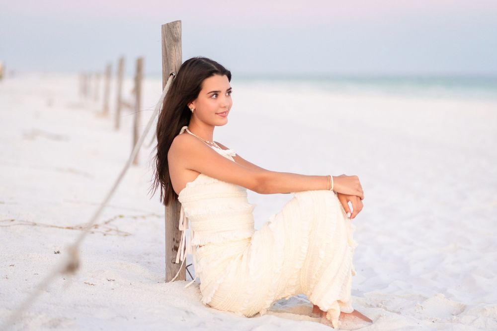 Person in flowing cream dress reclines on white sandy beach during golden hour.