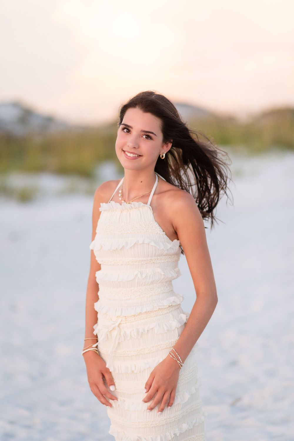 A series of beach portraits showing a person in a white ruffled dress with wind-blown hair against a coastal backdrop.