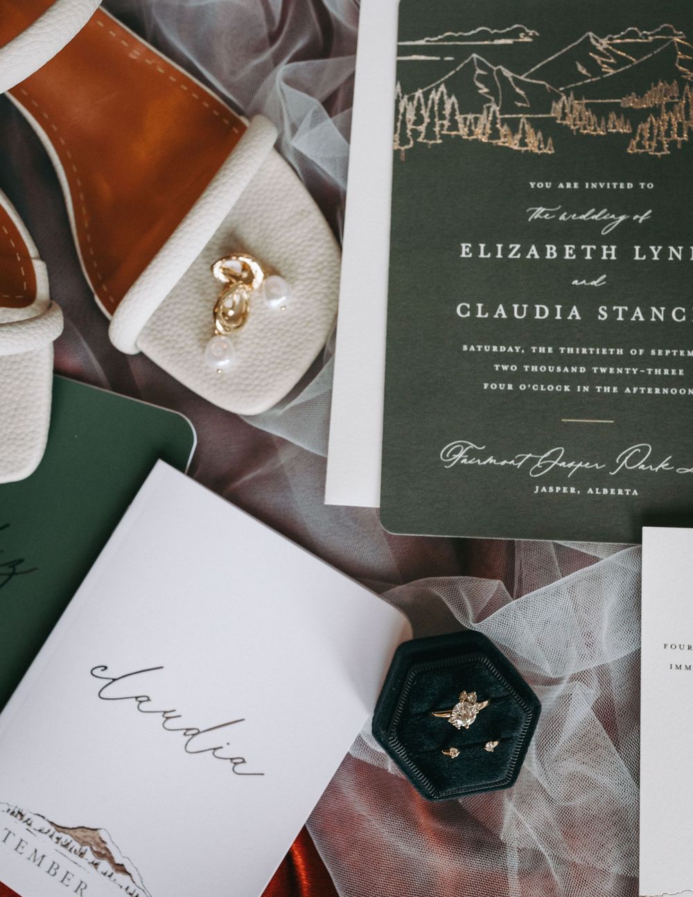 Wedding stationery set featuring dark green invitations and ring box on textured surface.