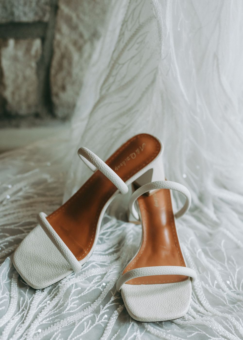 White bridal shoes with delicate straps arranged on a light fabric backdrop.