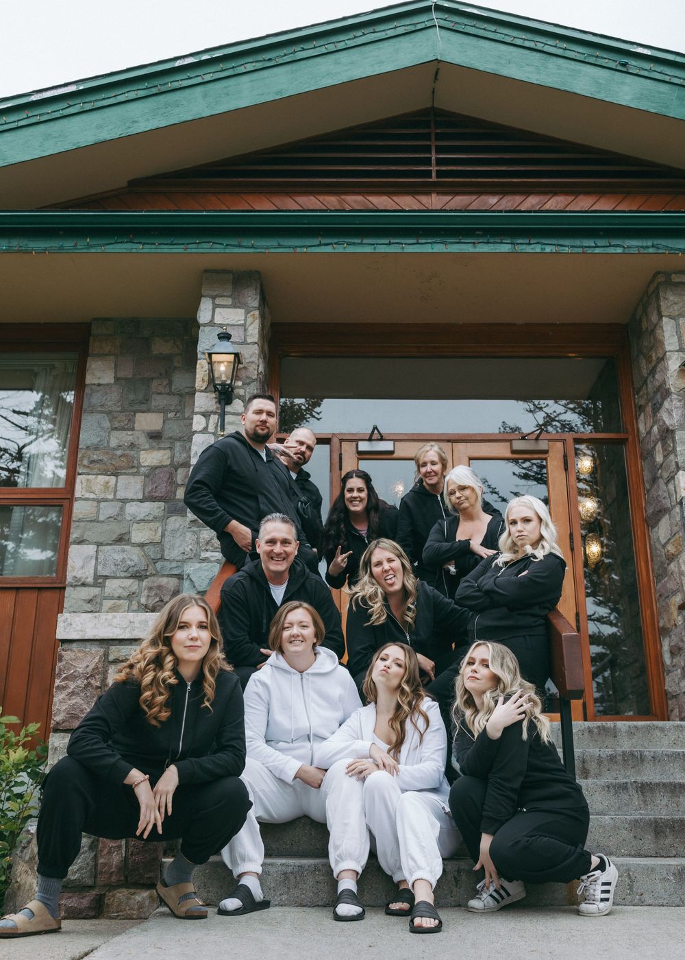 Group of friends in black and white outfits sitting and posing together on stone steps of a rustic building.