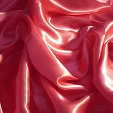 Close-up of rippled coral pink satin fabric creating a soft, luxurious texture pattern.