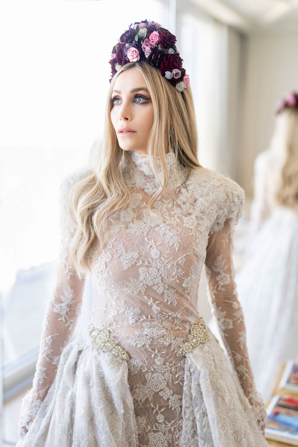 Elegant lace wedding dress with long sleeves and floral crown details in natural light.