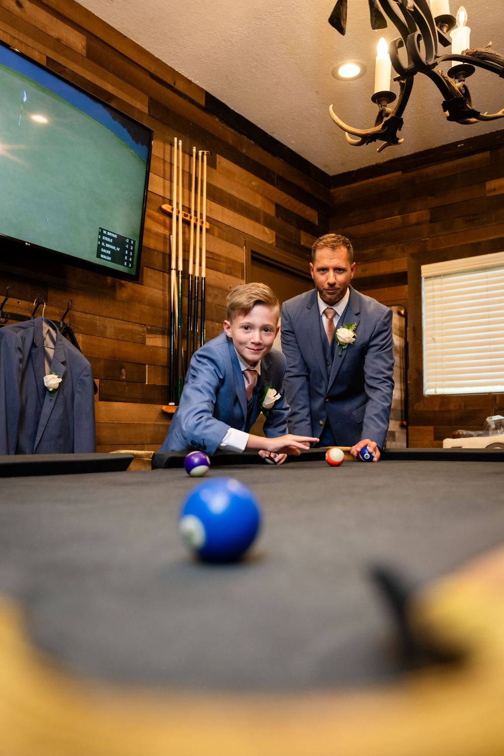 Wedding party playing pool in a wood-paneled game room.