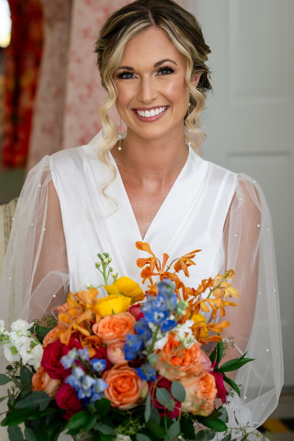 Bridal portrait with vibrant orange and blue wedding bouquet against light interior background.