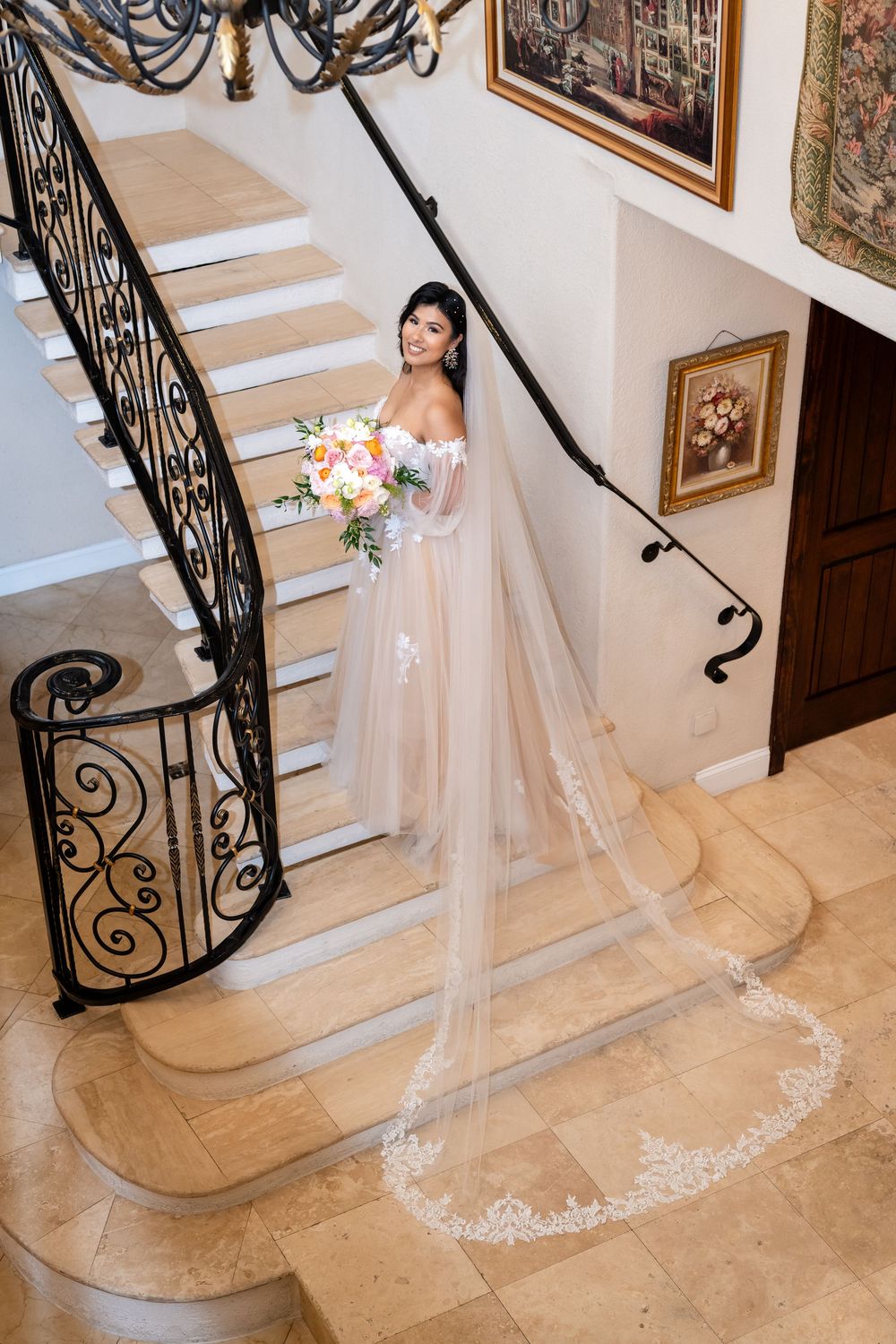 Elegant wedding dress with long lace train flowing down ornate staircase with wrought iron railings.