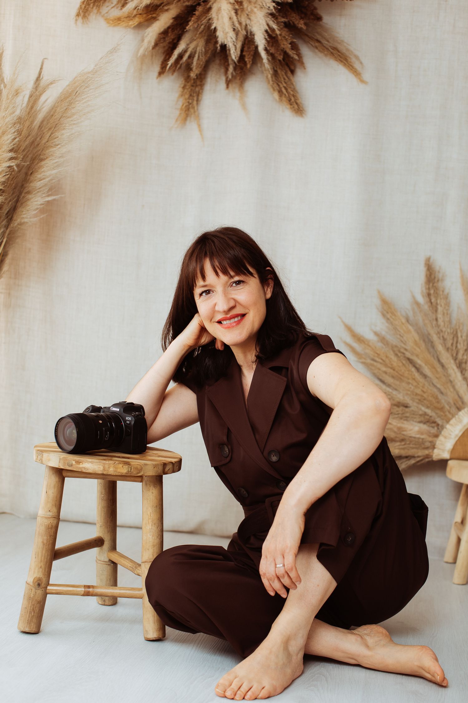 Studio portrait session with pampas grass decorations and wooden stool against light background.