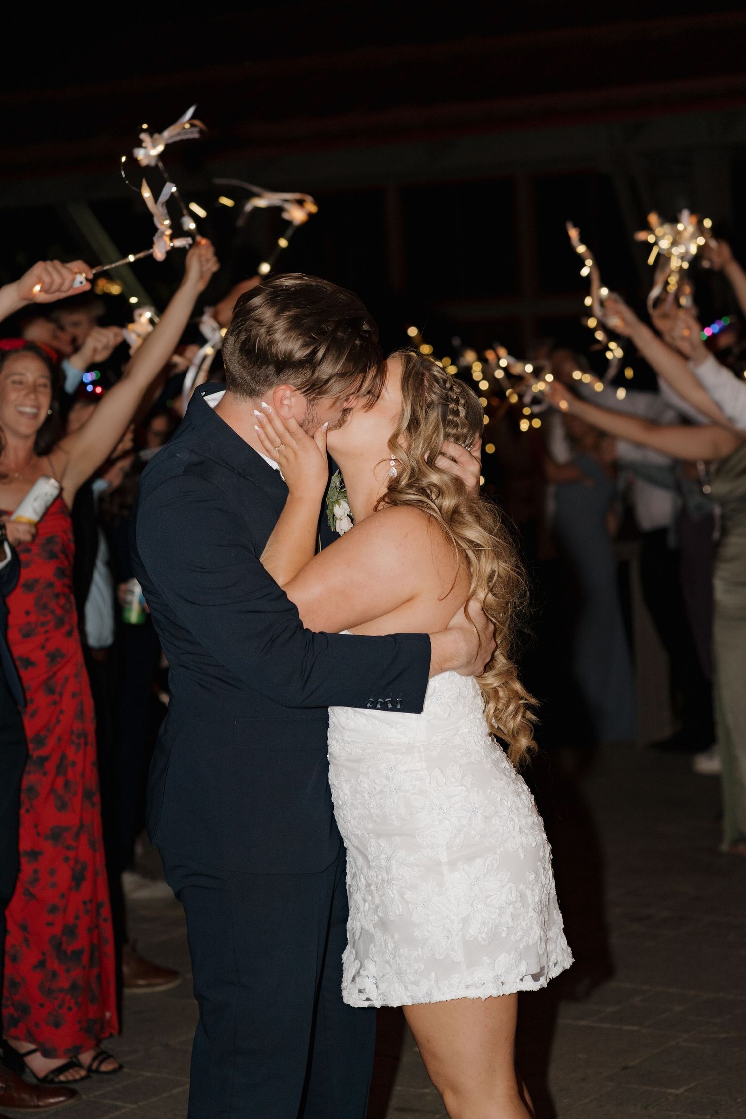 A couple shares an intimate dance moment at a wedding reception while guests wave sparklers in celebration.