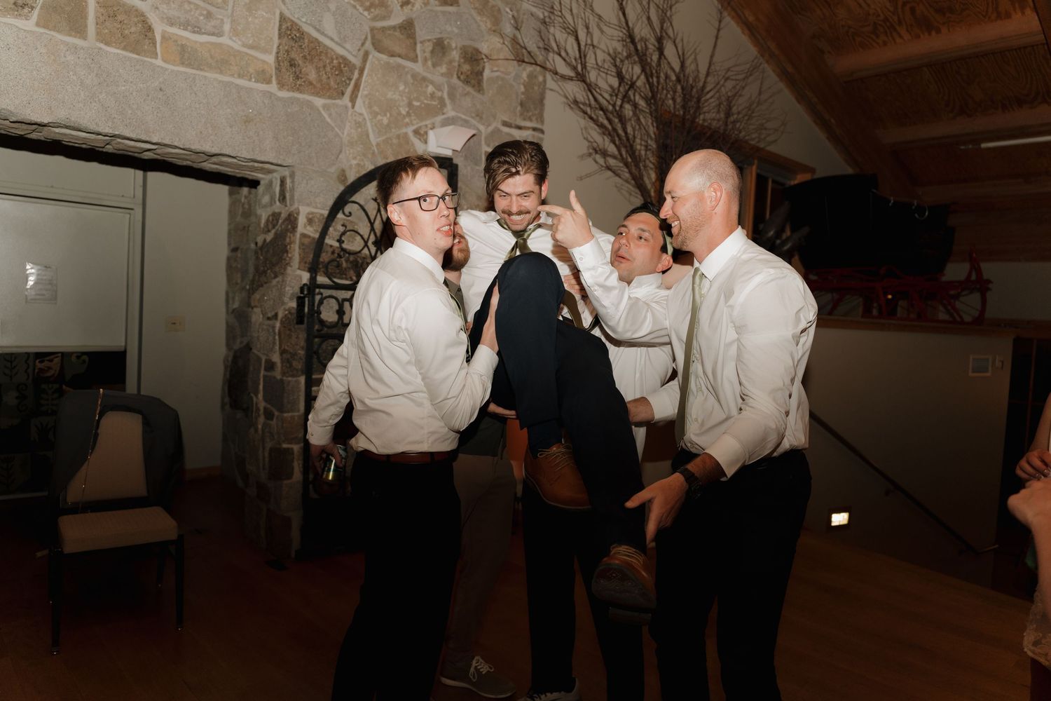 Wedding reception guests dancing and celebrating in a dimly lit rustic venue.