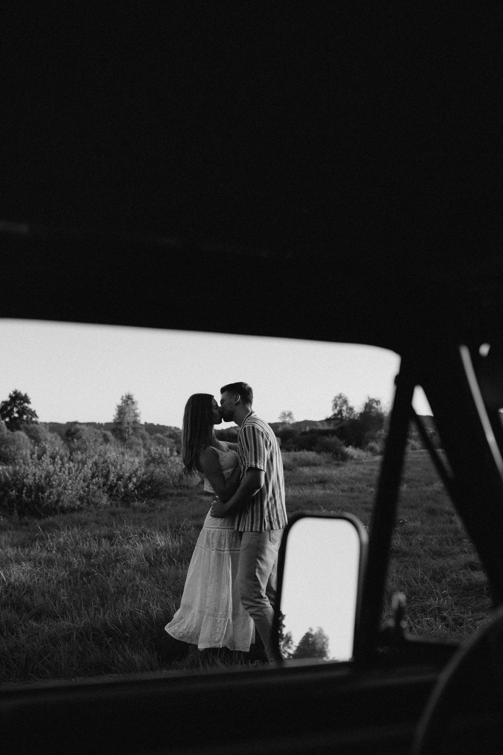 Black and white photos of a couple viewed through a car window in a scenic outdoor setting.