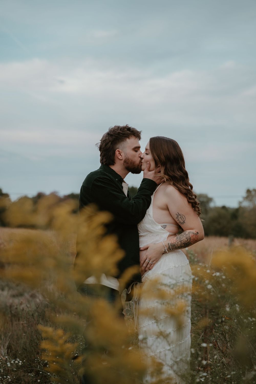 Couple sharing a kiss in wildflower field during outdoor maternity photo session.