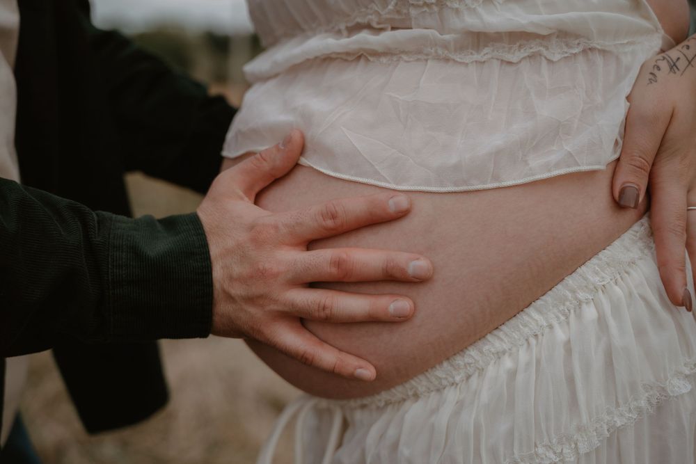 Close-up of couple's hands tenderly cradling pregnant belly during outdoor maternity photo session.