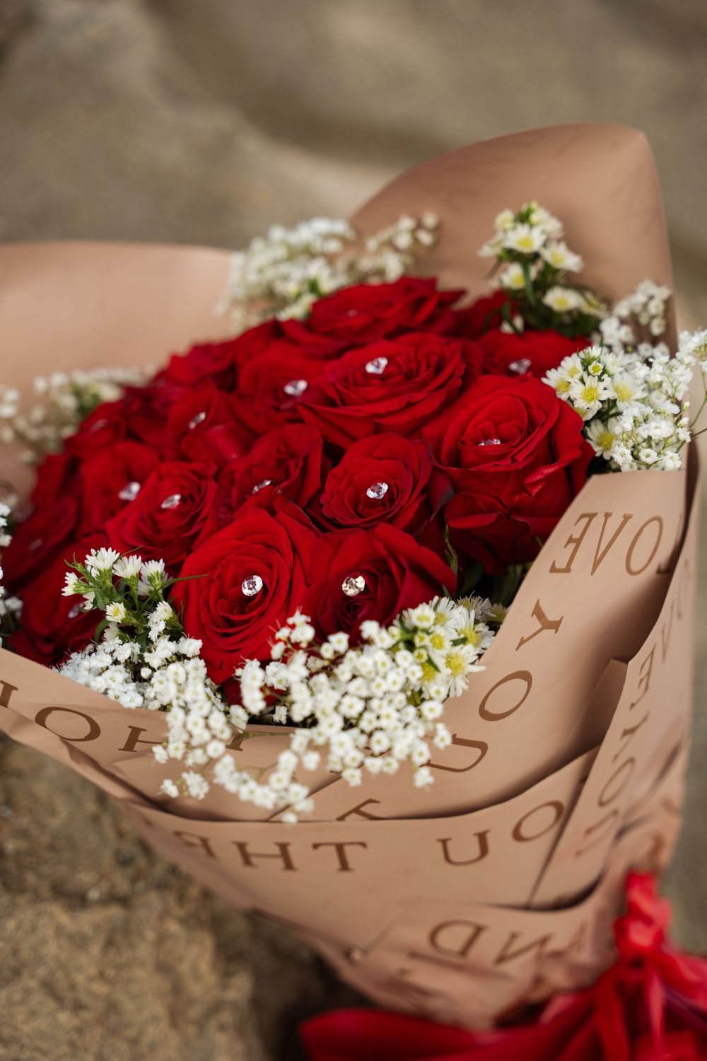 A bouquet of vibrant red roses wrapped in brown kraft paper with small white baby's breath flowers as accents.