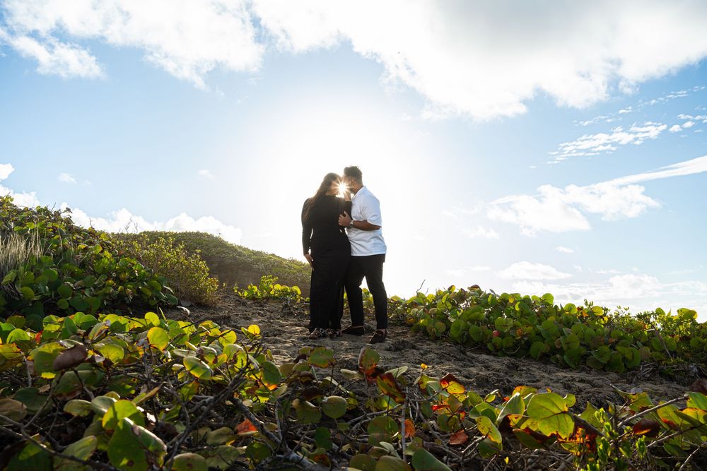 A couple stands on a mountain ridge overlooking a scenic landscape during sunset.