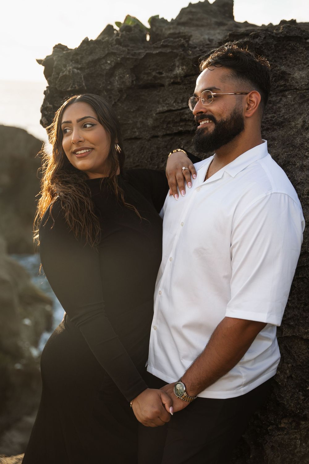 Couple in white shirts embracing against rocky cliffs during golden hour sunset.