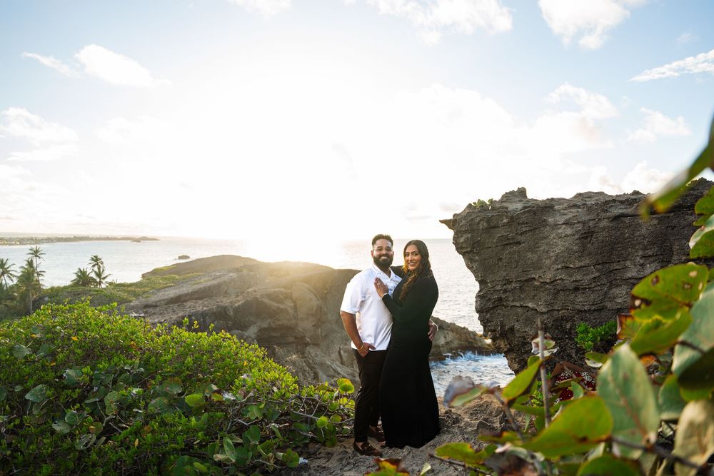 A scenic panoramic view of people exploring a rocky coastal cliff at sunset with ocean waves crashing below.