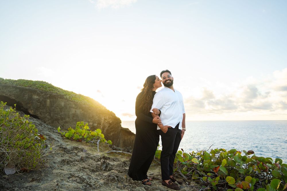 A couple embraces on a scenic coastal cliff during sunset while waves crash against the rocks below.
