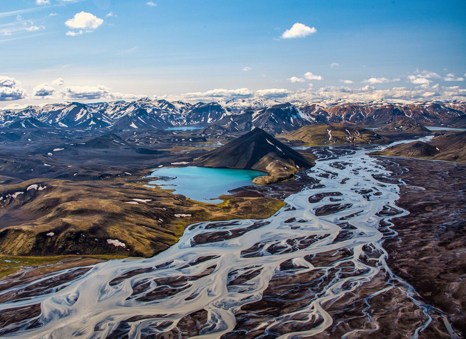 Aerial panorama of braided glacial rivers winding through snow-capped mountain valleys in Iceland.