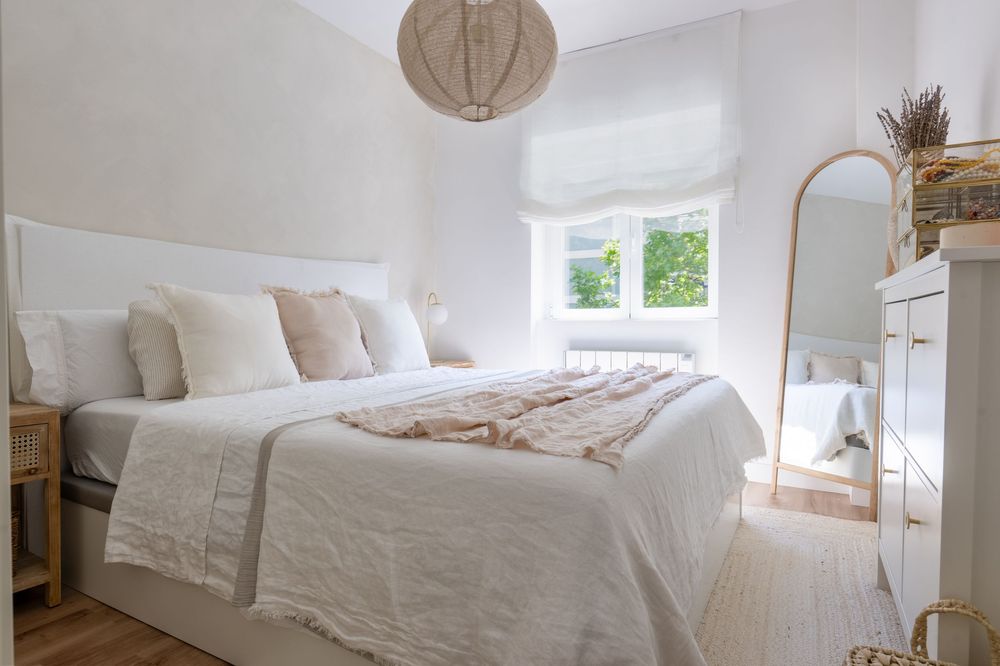 A bright and airy bedroom with white linen bedding, natural light, and rustic decor elements creates a serene atmosphere.