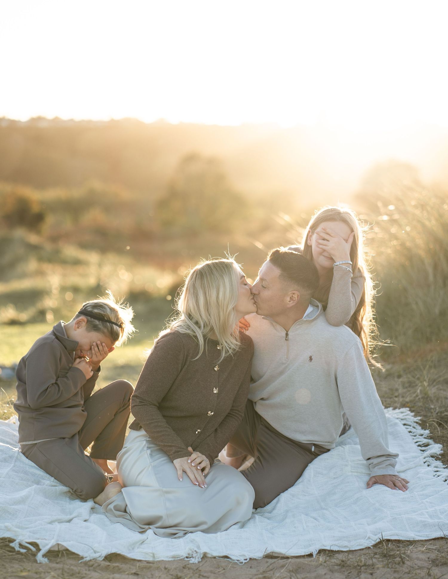 Romantic couple lying together on white blanket during golden hour sunset at beach.