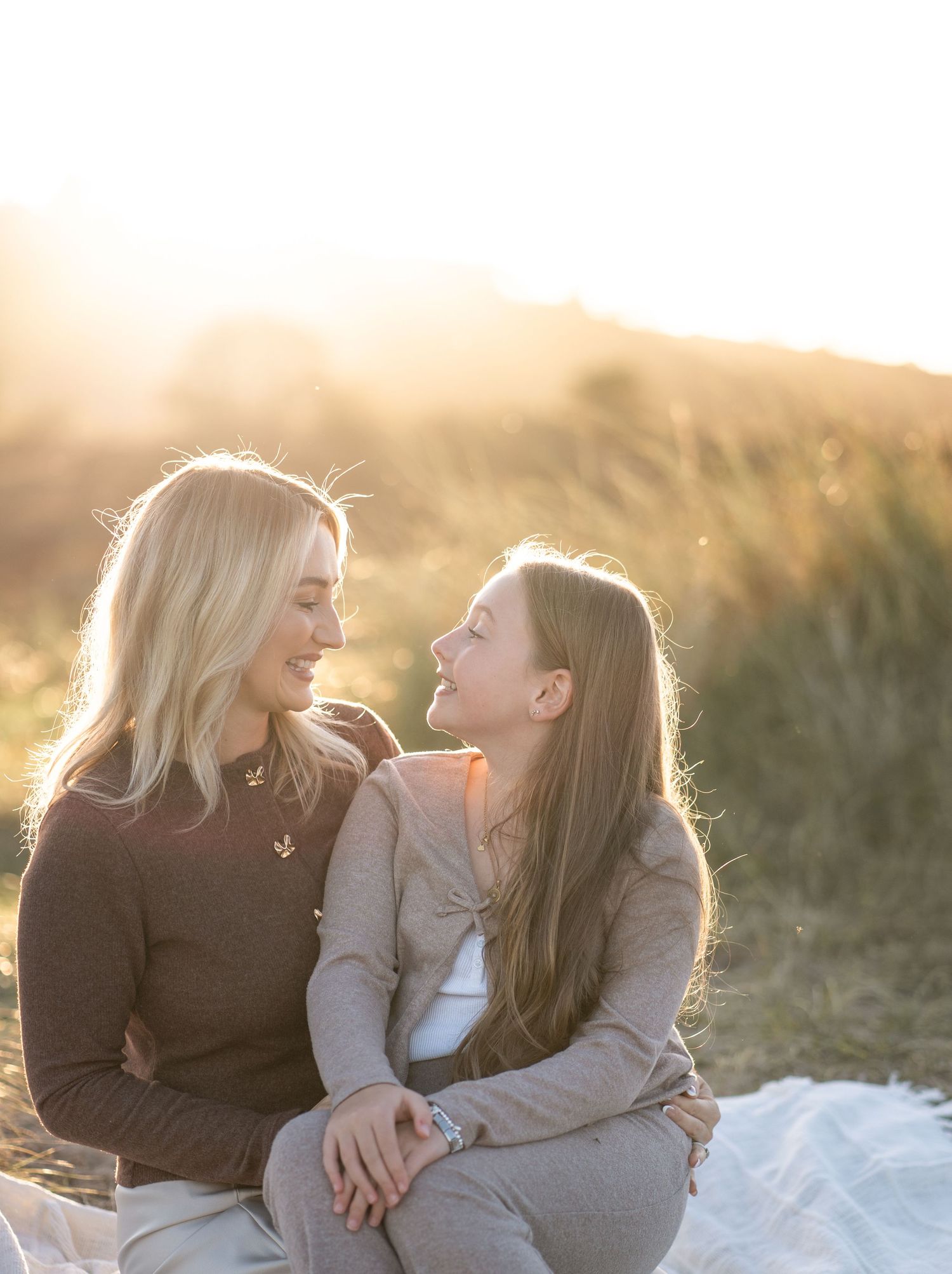 Mother and child share joyful laughter together outdoors during a warm sunset photoshoot.