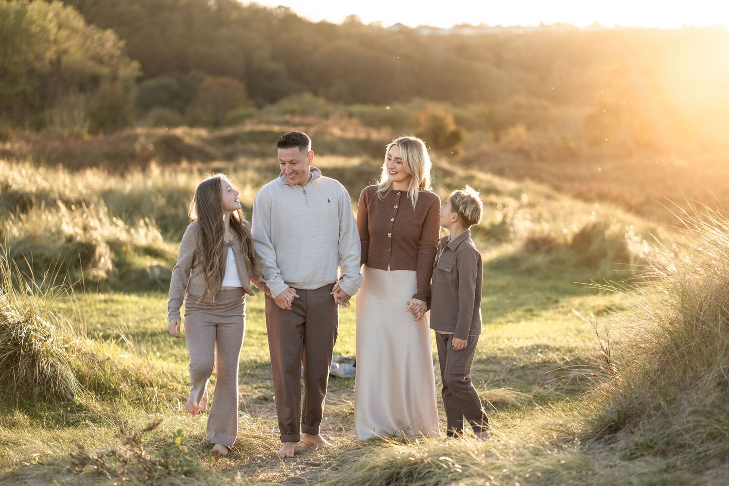 Family walking together through a golden field at sunset, holding hands and creating silhouettes against warm sunlight.